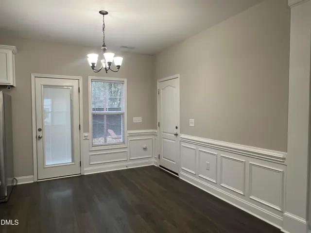 an empty room with wooden floor chandelier and windows