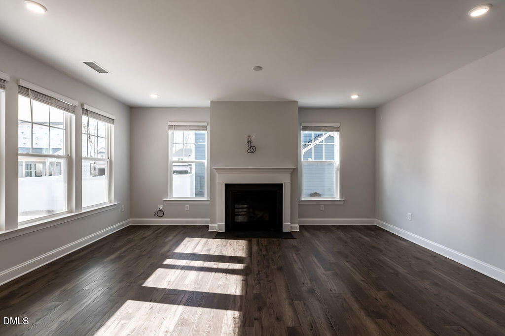 717 Ressler Street Holly Springs, NC 27540 - Photo 5 of 32 an empty room with windows a fireplace and wooden floor