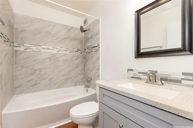 a bathroom with a granite countertop bathtub shower sink vanity mirror and toilet