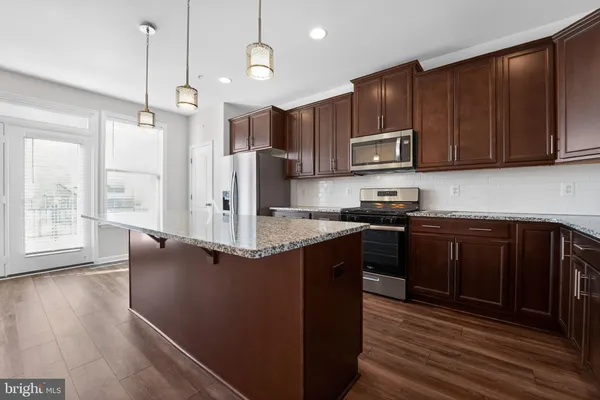a kitchen with kitchen island granite countertop wooden cabinets a stove a refrigerator and a microwave with wooden floor