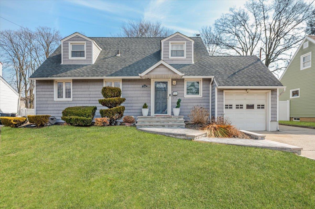 1747 Meadowbrook Road Merrick, NY 11566 - Photo 1 of 1 New england style home with driveway, a shingled roof, a front lawn, and an attached garage