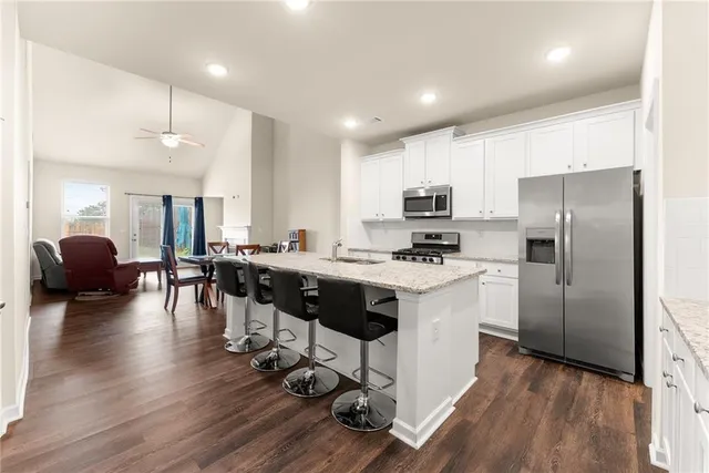 a kitchen with granite countertop a refrigerator a stove a sink a dining table and chairs with wooden floor