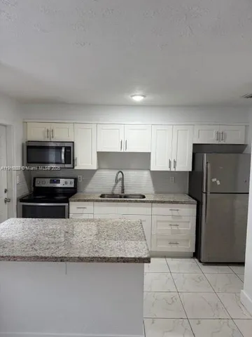 a kitchen with granite countertop a refrigerator and a stove top oven