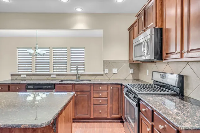 a kitchen with stainless steel appliances granite countertop a sink a stove and a wooden cabinets