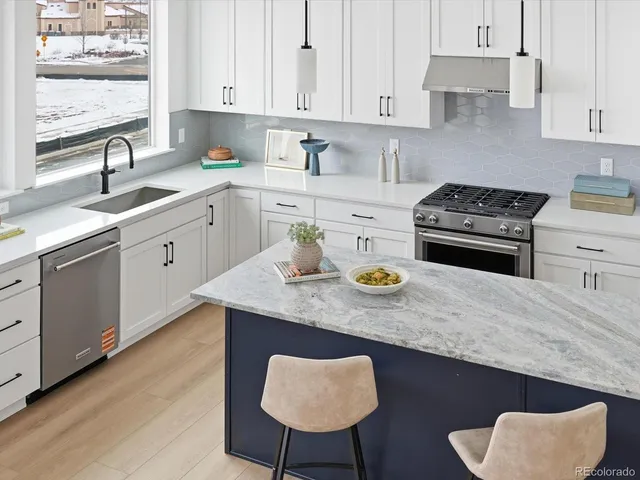 a kitchen with stainless steel appliances a sink a stove a refrigerator white cabinets and wooden floor