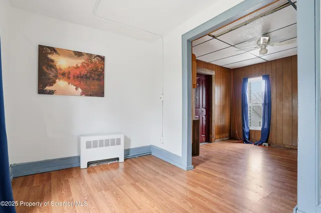 a view of an empty room with wooden floor and a ceiling fan