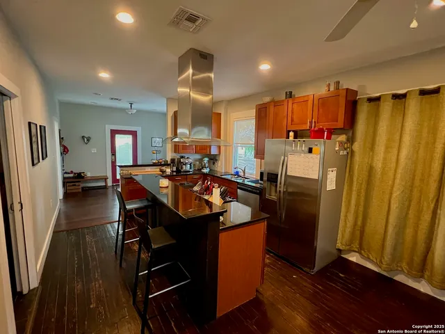 a kitchen with stainless steel appliances a refrigerator a sink dishwasher a stove and a dining table with wooden floor