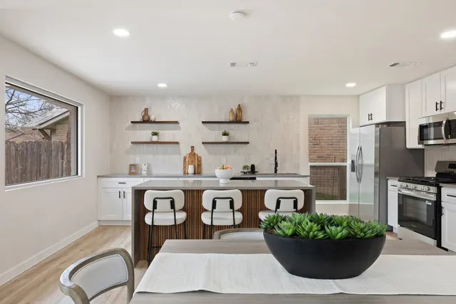 a kitchen with stainless steel appliances granite countertop a dining table chairs stove and refrigerator