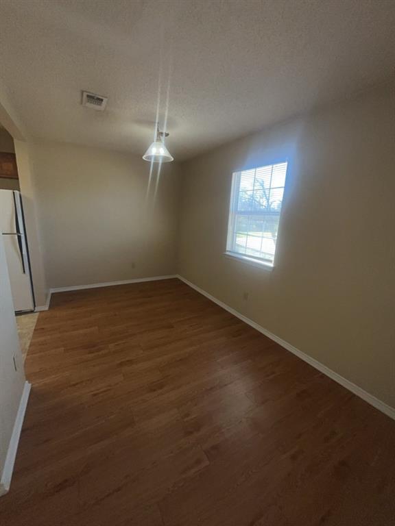 125 Northeast Johnson Avenue, Unit 30 Burleson, TX 76028 - Photo 12 of 13 Unfurnished dining area with baseboards, visible vents, a textured ceiling, and wood finished floors