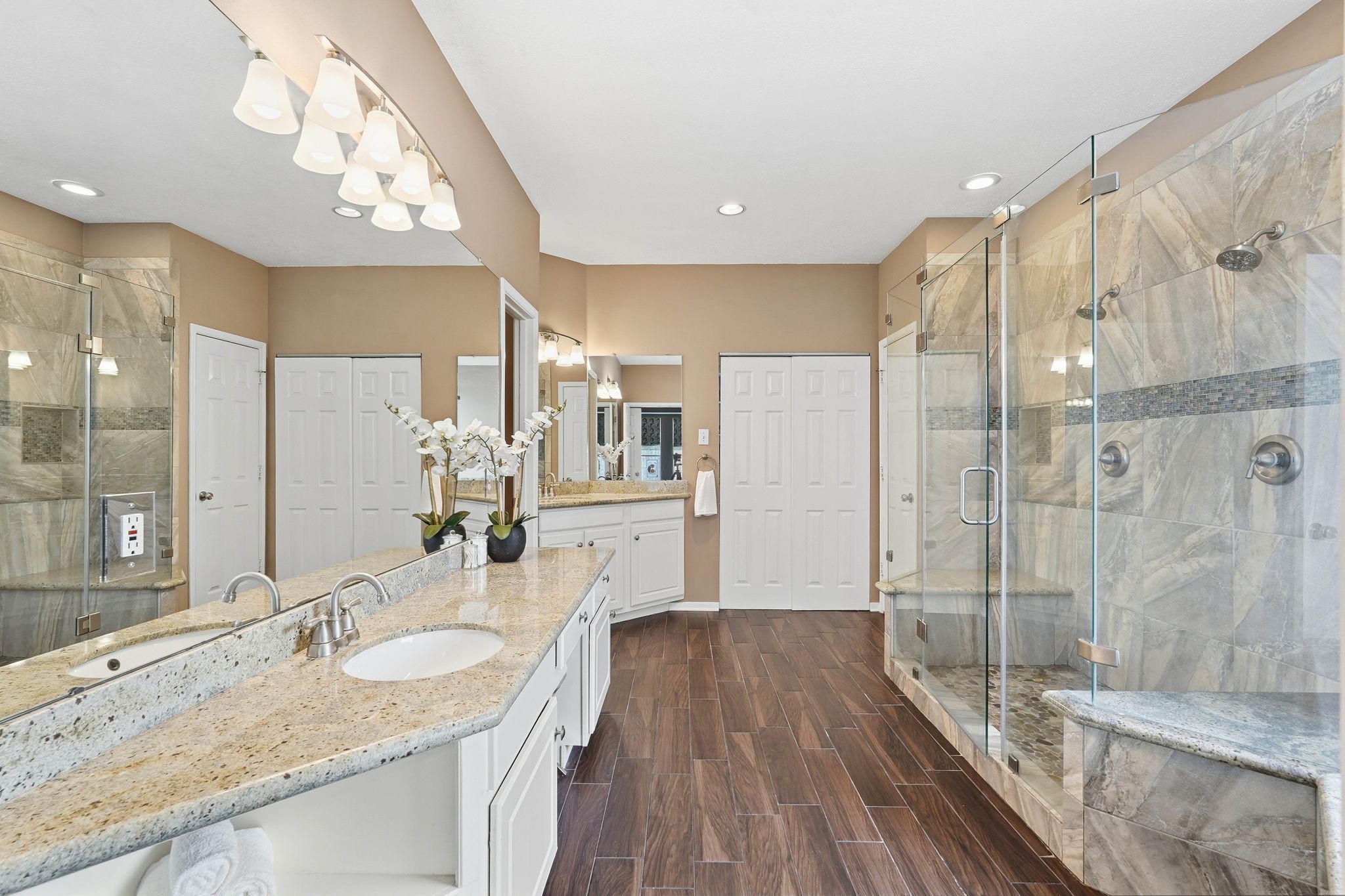 2515 Woodsboro Drive Spring, TX 77388 - Photo 19 of 44 This spacious primary bathroom features a large granite double vanity, elegant lighting, and a roomy glass-enclosed shower with stylish tilework. The warm wood tile flooring and neutral tones create a welcoming atmosphere.