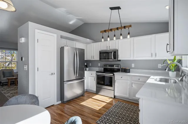 a kitchen with stainless steel appliances granite countertop a refrigerator a sink dishwasher a stove and white cabinets with wooden floor