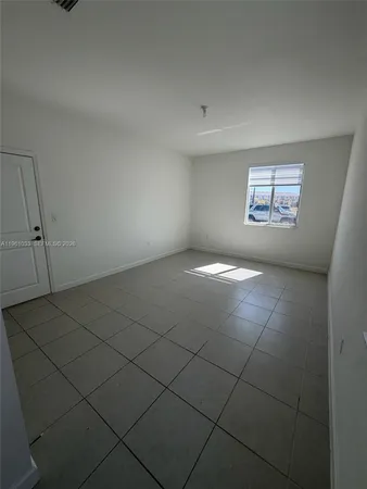 an empty room with windows and way to kitchen