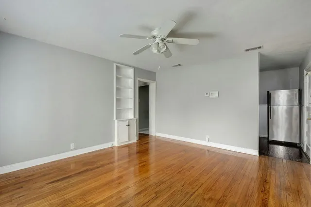 a view of an empty room with wooden floor and a ceiling fan