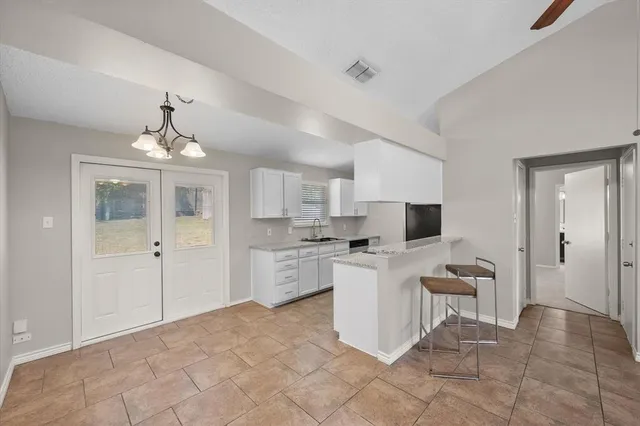 a view of a kitchen with kitchen island white cabinets a sink a window and stainless steel appliances
