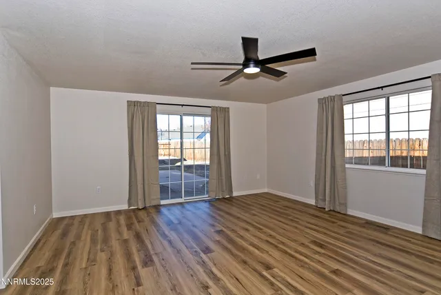 an empty room with wooden floor fan and windows