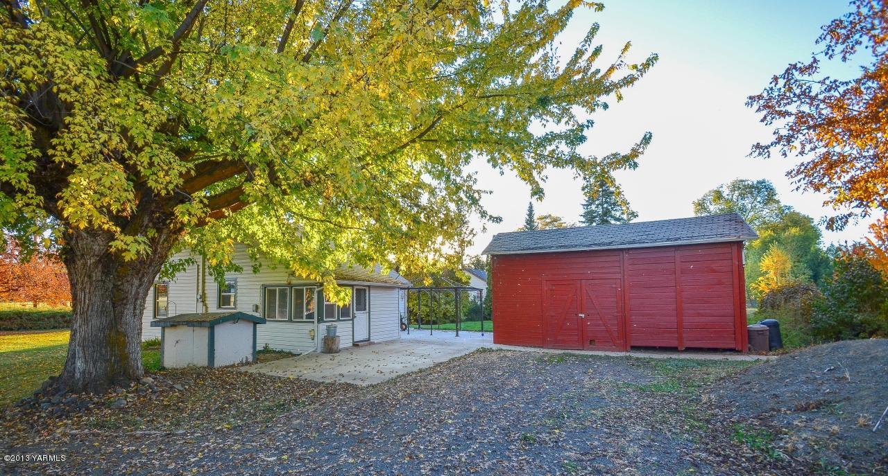 11703 Gilbert Road Yakima, WA 98903 - Photo 10 of 12 a view of a backyard with large trees and brick wall