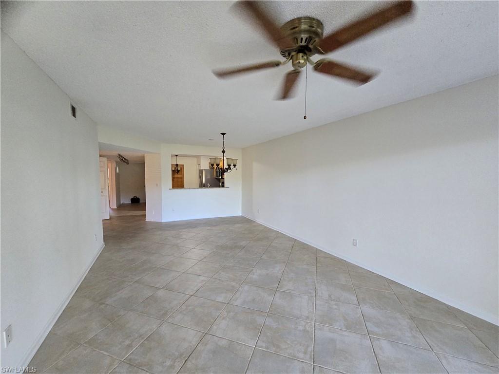 5737 Whitaker Road, Unit C104 Naples, FL 34112 - Photo 8 of 34 Unfurnished living room with ceiling fan with notable chandelier, a textured ceiling, and light tile patterned flooring