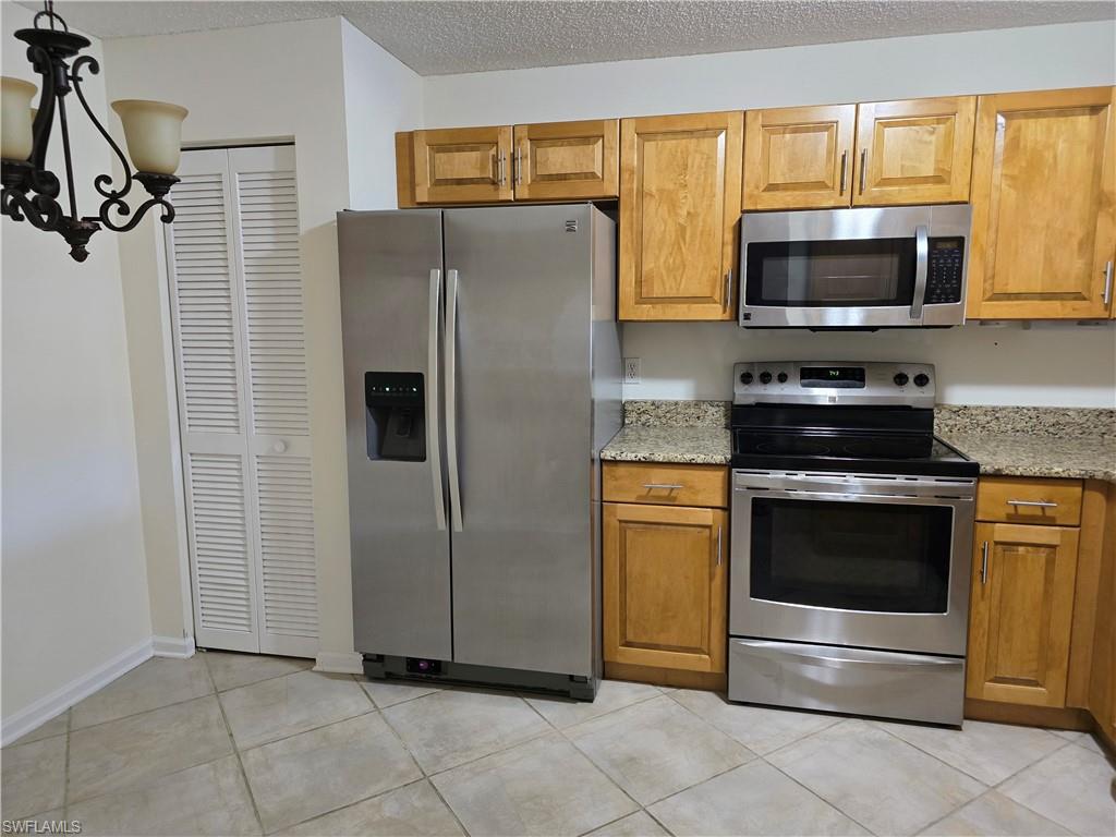 5737 Whitaker Road, Unit C104 Naples, FL 34112 - Photo 9 of 34 Kitchen featuring appliances with stainless steel finishes, a notable chandelier, granite countertops, a textured ceiling, and light tile patterned flooring