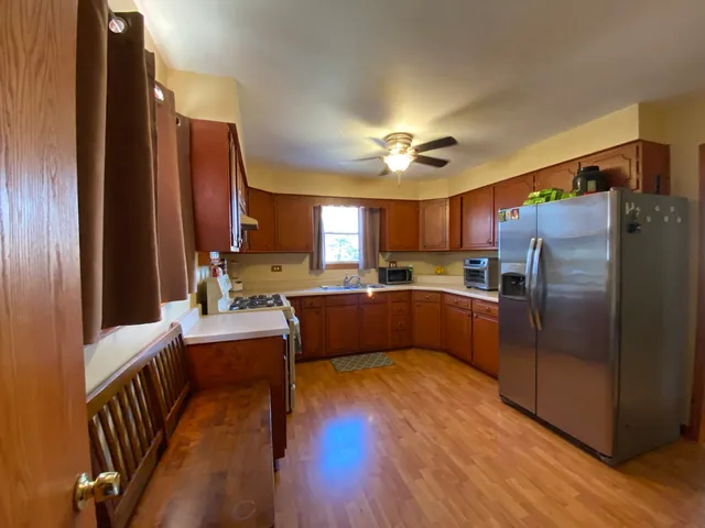 a kitchen with stainless steel appliances granite countertop a refrigerator a sink dishwasher a stove and white countertops with wooden floor