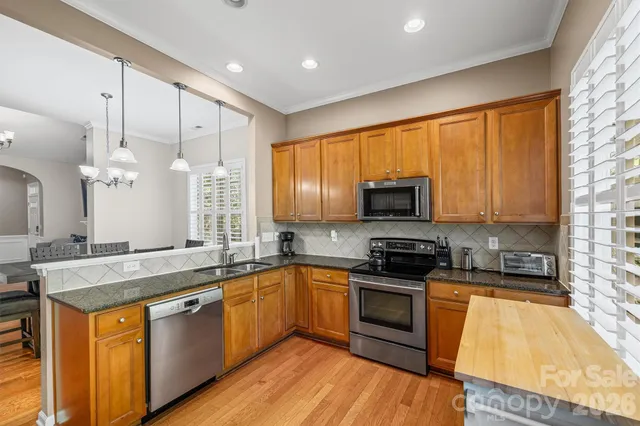 a kitchen with stainless steel appliances granite countertop wooden cabinets a sink a stove a refrigerator and island with wooden floor