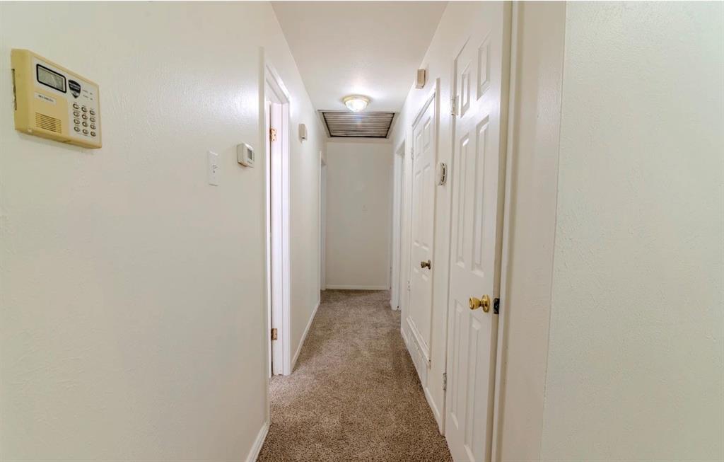 8017 Woodhue Road Dallas, TX 75228 - Photo 10 of 20 Carpeted hallway with white interior doors, a security panel, and a ceiling-mounted light fixture