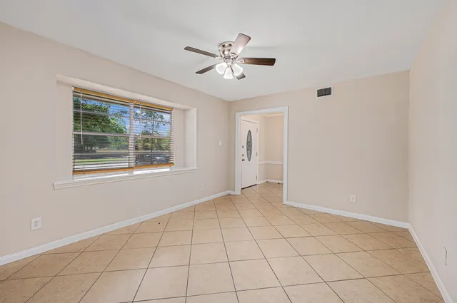 a view of an empty room with window and chandelier fan