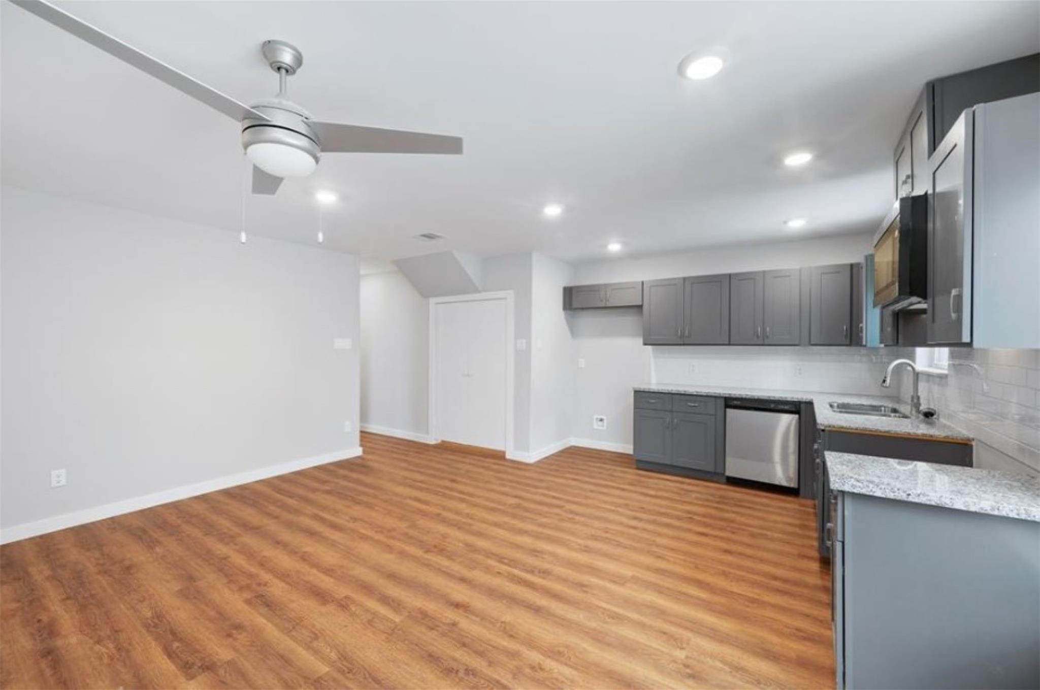 8120 Laura Koppe Road, Unit B Houston, TX 77028 - Photo 5 of 25 This photo showcases a modern, open-concept kitchen and living area with sleek gray cabinetry, stainless steel appliances, wood laminate flooring, and a ceiling fan, creating a spacious and contemporary living space.