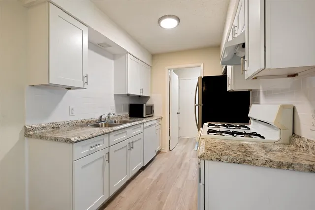 a kitchen with stainless steel appliances granite countertop a stove top oven a sink a refrigerator and white cabinets