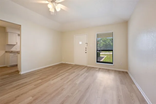 an empty room with wooden floor a ceiling fan and windows