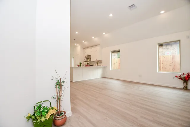 a view of an empty room and kitchen with wooden floor