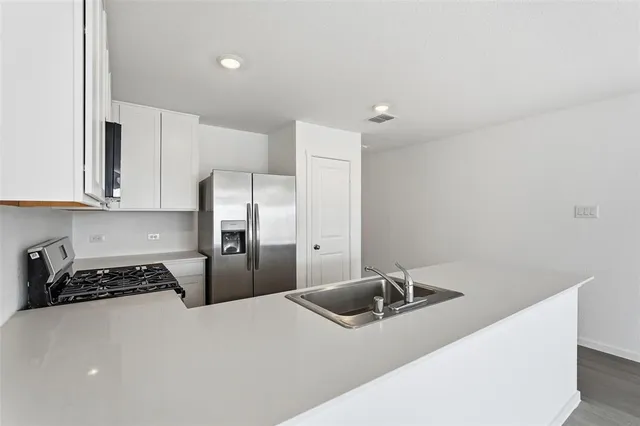 a kitchen with stainless steel appliances a refrigerator a sink a stove and white cabinets