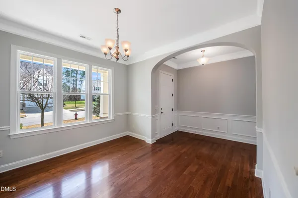 an empty room with wooden floor chandelier and windows