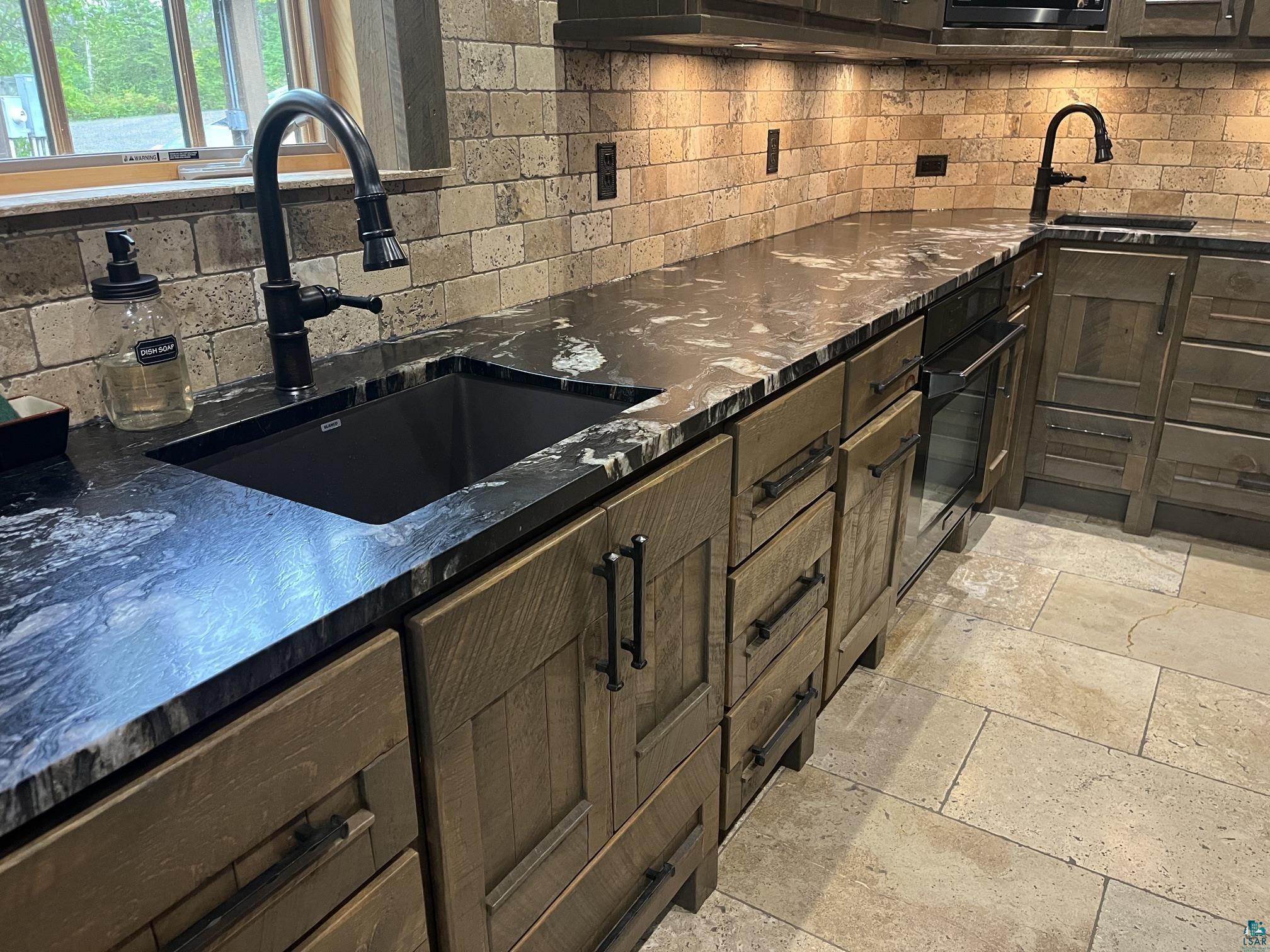 70745 Range Line Road Iron River, WI 54847 - Photo 3 of 40 Black granite countertops, undermount sink with matte black faucet, wood-finish cabinetry, stone tile flooring, and stone tile backsplash