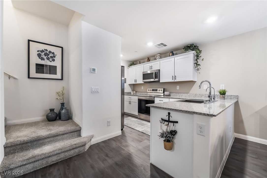 12235 Glass Desert Road, Unit 2 Las Vegas, NV 89183 - Photo 11 of 33 Kitchen with stainless steel appliances, white cabinets, light stone counters, a peninsula, and dark wood finished floors