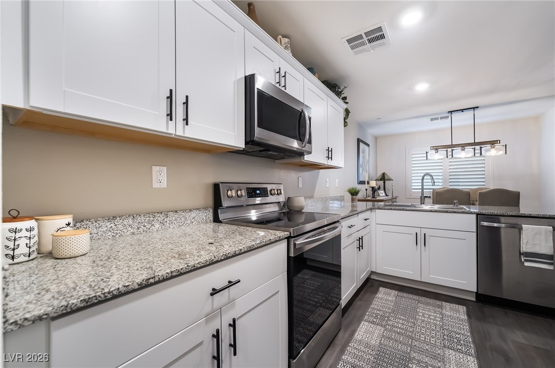 12235 Glass Desert Road, Unit 2 Las Vegas, NV 89183 - Photo 9 of 33 Kitchen featuring stainless steel appliances, light stone countertops, white cabinetry, pendant lighting, and dark wood finished floors