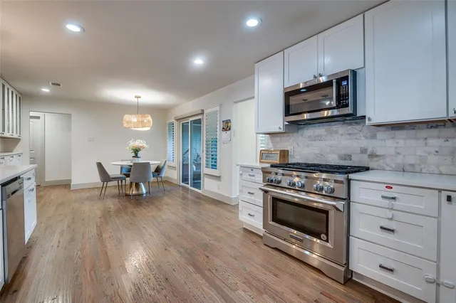 a kitchen with stainless steel appliances granite countertop a stove top oven a sink dishwasher a dining table and chairs with wooden floor