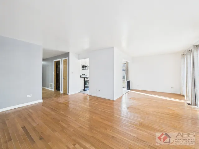 a view of an empty room with wooden floor and windows