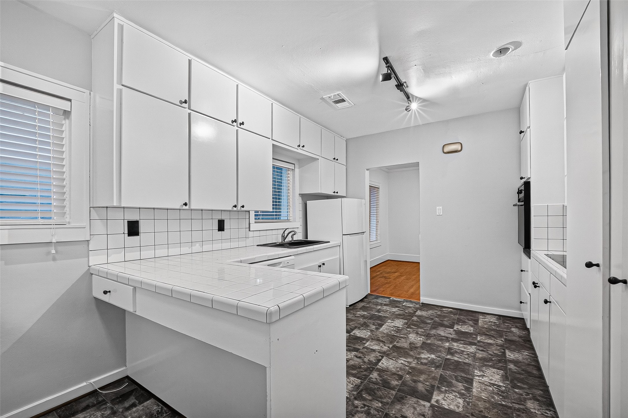 1758 Hawthorne Street, Unit 2 Houston, TX 77098 - Photo 8 of 19 Modern kitchen with sleek black granite countertops and white cabinetry. Features tiled backsplash, built-in appliances, and ample storage. Open doorway leads to a room with wood flooring, enhancing the space's flow.