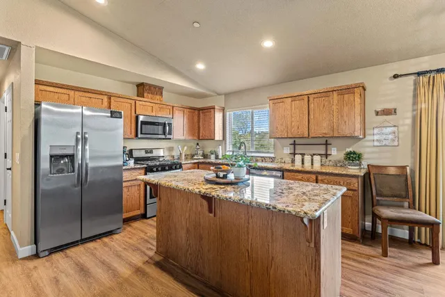 a kitchen with stainless steel appliances granite countertop a refrigerator a stove a sink a oven and a refrigerator with wooden floor