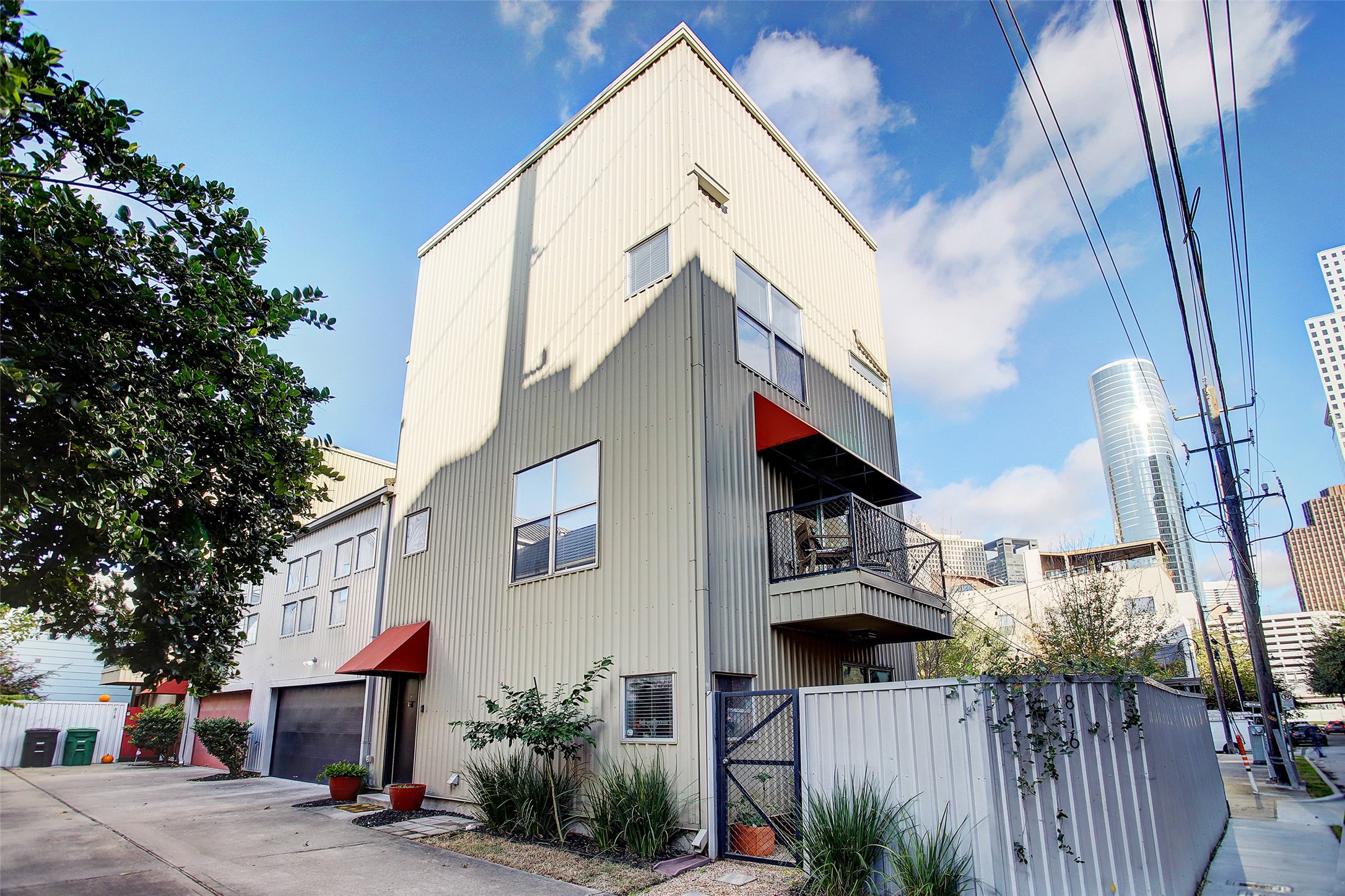 816 Ruthven Street Houston, TX 77019 - Photo 2 of 39 Modern three-story townhouse with a sleek exterior, featuring red awnings and a small balcony. Located in an urban setting with cityscape views.
