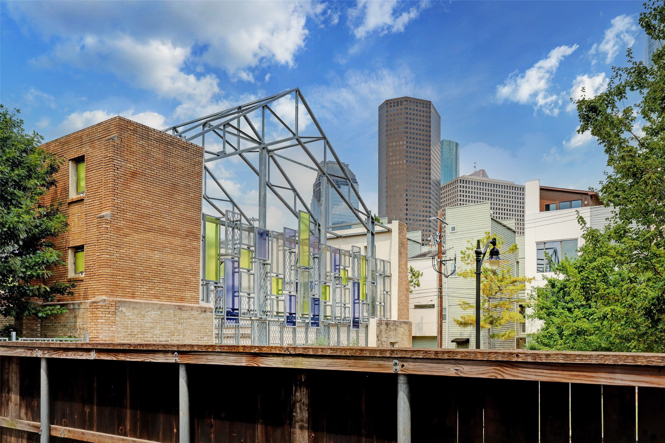 816 Ruthven Street Houston, TX 77019 - Photo 37 of 39 Modern urban setting with a mix of brick and contemporary architecture. The area features artistic structures and is framed by a clear blue sky with city skyline views, suggesting a vibrant neighborhood.
