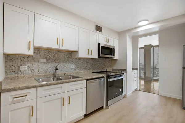 a kitchen with stainless steel appliances granite countertop white cabinets a sink a stove a refrigerator and a microwave