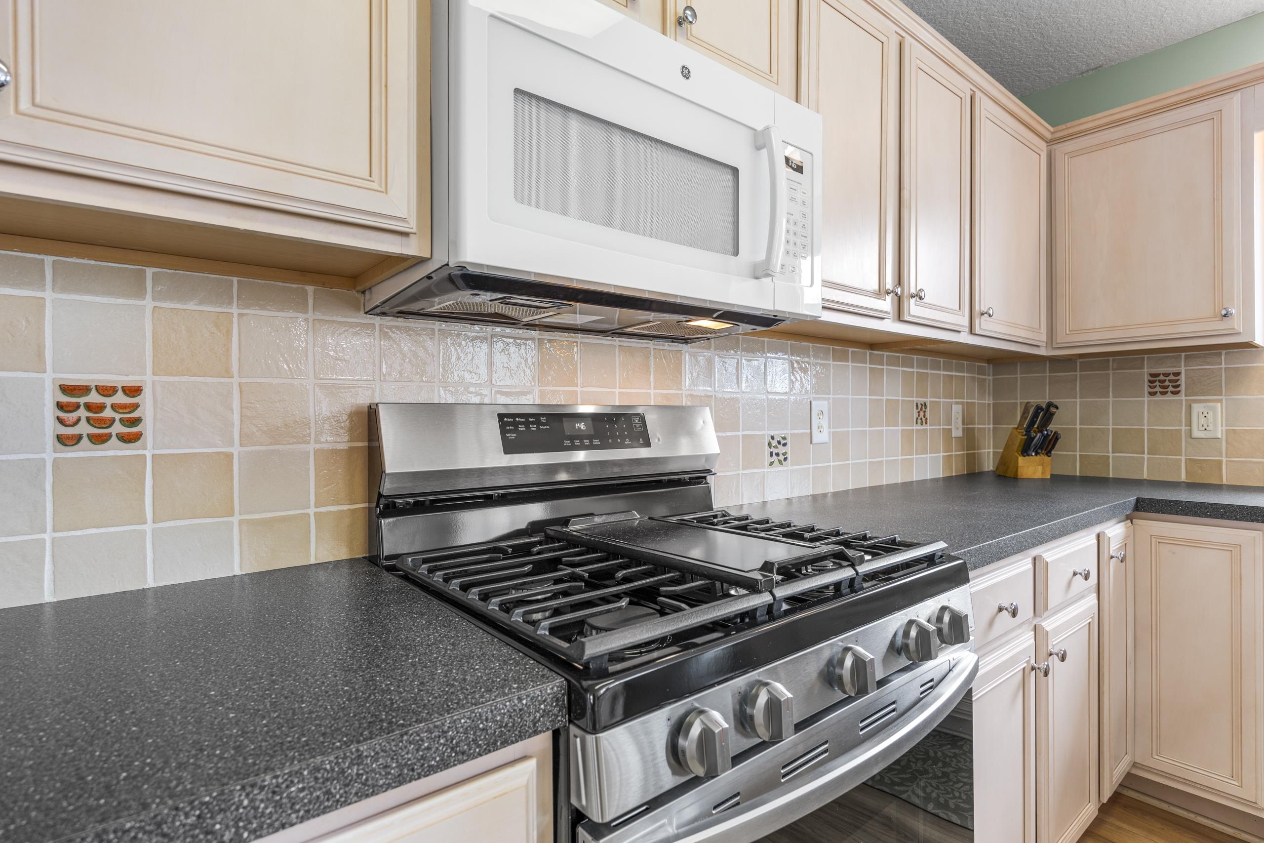 722 Downing Court Longs, SC 29568 - Photo 10 of 40 Kitchen featuring stainless steel gas range, dark countertops, white microwave, a textured ceiling, and backsplash