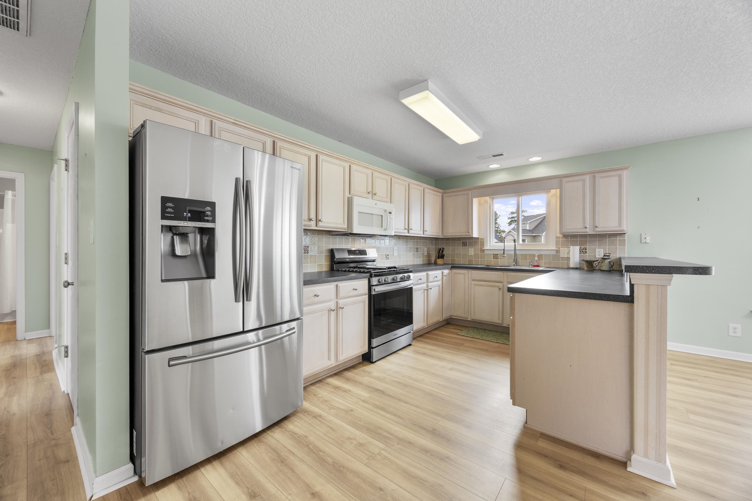 722 Downing Court Longs, SC 29568 - Photo 12 of 40 Kitchen with dark countertops, stainless steel appliances, a peninsula, light wood-style flooring, and tasteful backsplash