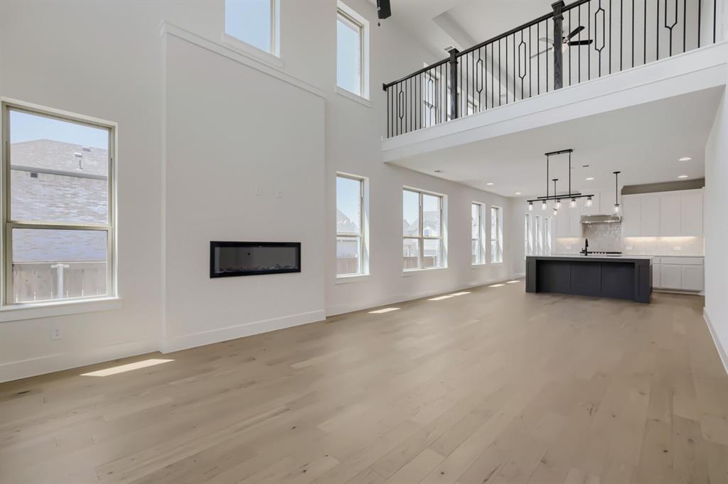 824 Stone Grv Road Lavon, TX 75166 - Photo 4 of 26 Open-concept living area featuring light wood-finish flooring, a wall-mounted linear fireplace, and an expansive kitchen with a dark-toned island and light cabinetry