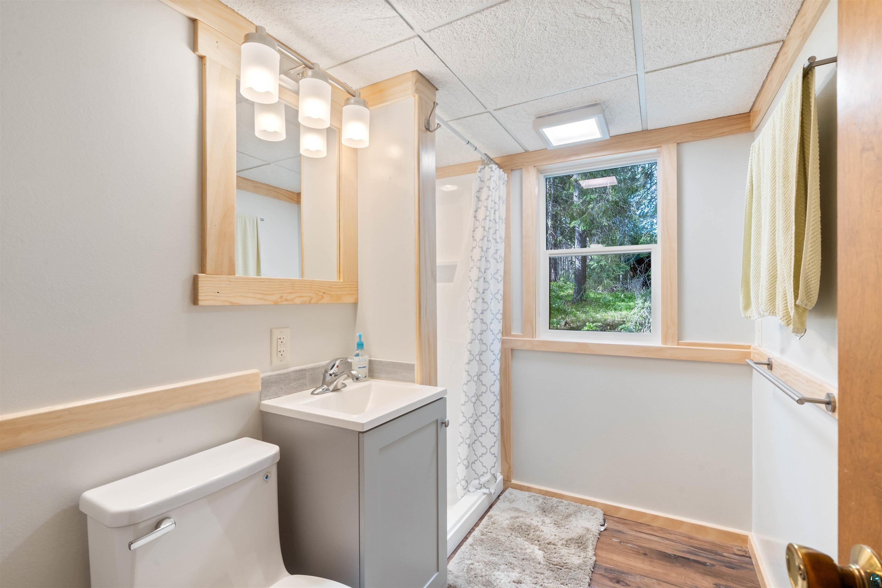 4793 Anderson Road Hermantown, MN 55811 - Photo 16 of 39 Bathroom featuring wood-finish flooring, a contemporary vanity with an integrated sink, a built-in shower stall, a single window, and light wood trim throughout
