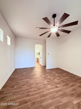 a view of an empty room with wooden floor and a ceiling fan