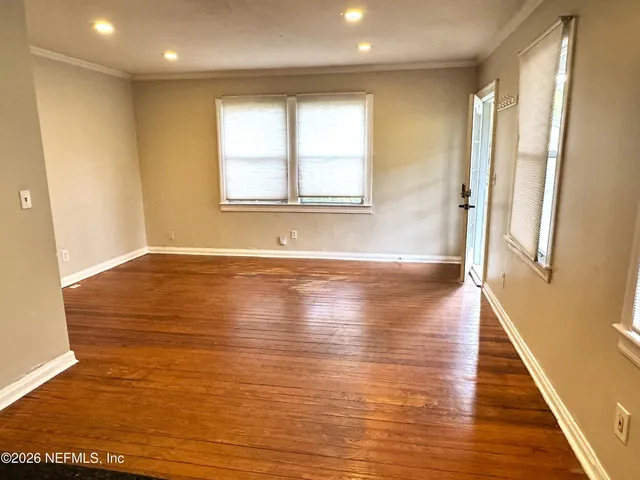 a view of an empty room with wooden floor and a window