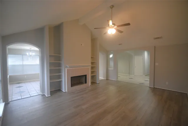 an empty room with wooden floor fireplace and windows