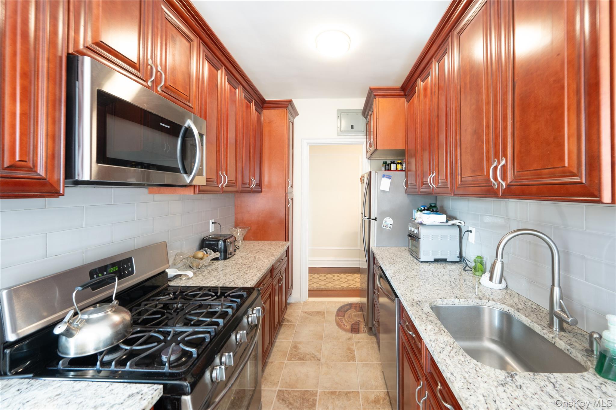 1468 Midland Avenue, Unit 4D Bronxville, NY 10708 - Photo 13 of 24 Kitchen featuring appliances with stainless steel finishes, backsplash, light stone counters, and light tile patterned floors